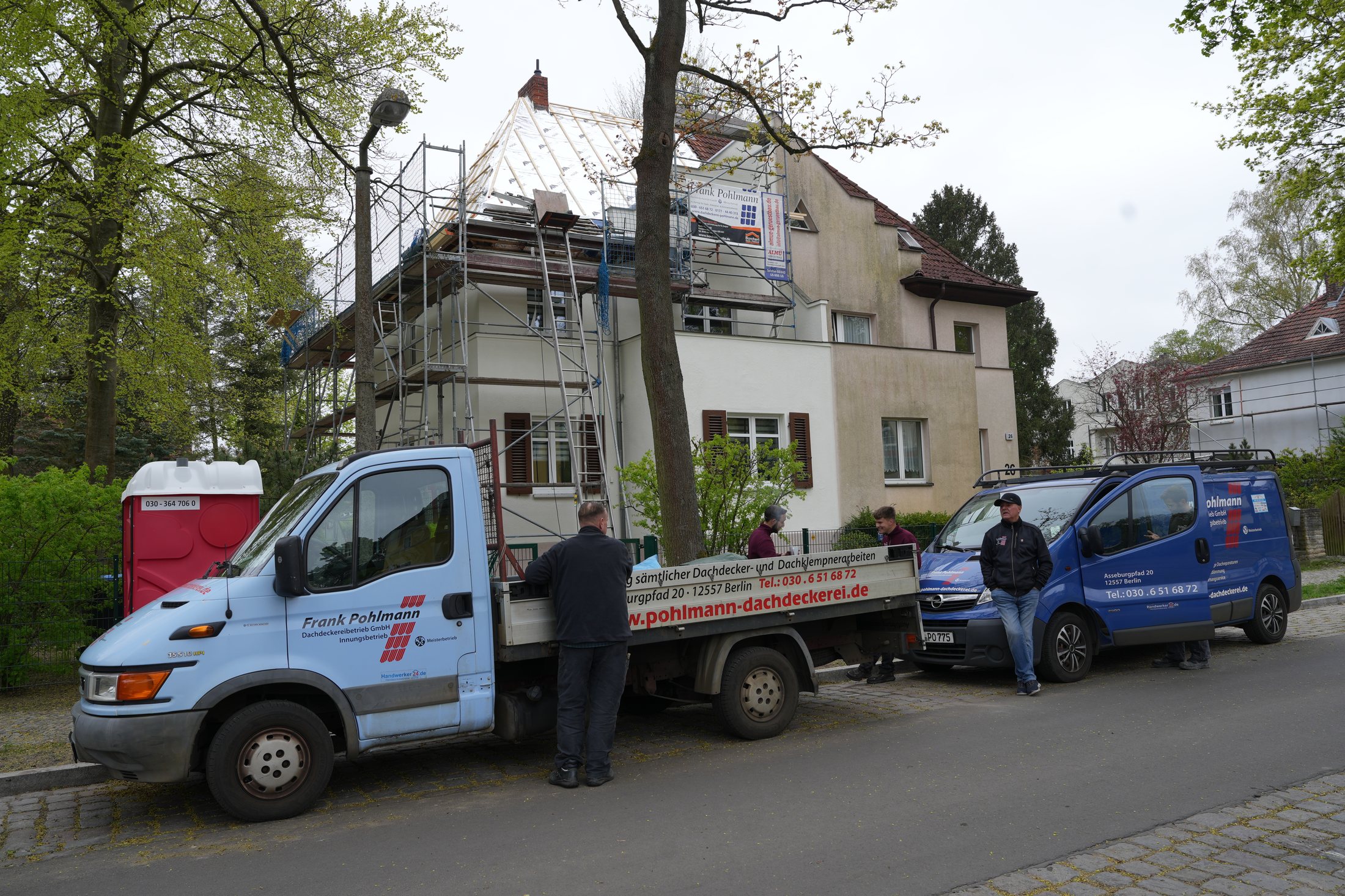 Pohlmann Dachdeckerei – Team mit Firmenfahrzeugen vor einer Berliner Baustelle